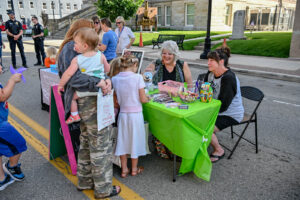 Children choosing giveaways at a table on Main Street in New Lexington during the 2026 Chalk It Up to Summer event for kids and families.