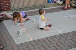Two small children drawing with chalk on Main Street in New Lexington during the 2026 Chalk It Up to Summer event for kids and families.