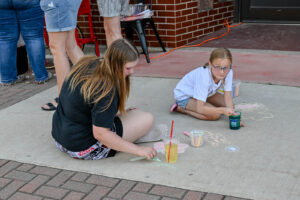 Children drawing with chalk and enjoying treats on Main Street in New Lexington during the 2026 Chalk It Up to Summer event for kids and families.