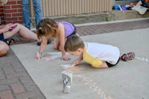 Two children drawing on the sidewalk on Main Street in New Lexington during the 2026 Chalk It Up to Summer event for kids and families.