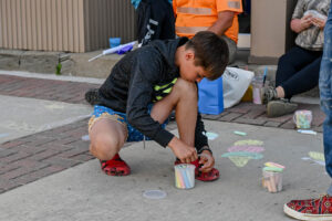 Young man drawing with chalk on Main Street in New Lexington during the 2026 Chalk It Up to Summer event for kids and families.