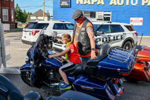 Young boy sitting on a motorcycle with a member of the New Lex Riders on Main Street in New Lexington during the 2026 Chalk It Up to Summer event for kids and families.