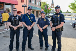 Four members of the New Lexington Fire and Police departments on Main Street in New Lexington during the 2026 Chalk It Up to Summer event for kids and families.
