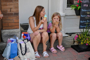 Mother and daughter enjoy ice cream on a stoop outside Happy Cones on Main Street in New Lexington during the 2026 Chalk It Up to Summer event for kids and families.
