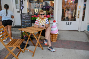 Woman sitting at a table outside Happy Cones on Main Street in New Lexington during the 2026 Chalk It Up to Summer event for kids and families.