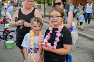 Girls wearing leis they chose on Main Street in New Lexington during the 2026 Chalk It Up to Summer event for kids and families.