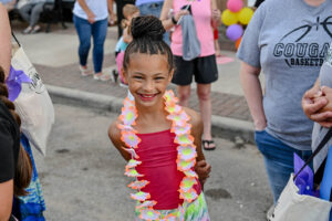 Girl smiling and wearing a lei she chose on Main Street in New Lexington during the 2026 Chalk It Up to Summer event for kids and families.